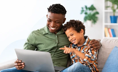Pai sorrindo ao lado do filho, os dois olhando juntos para a tela de um notebook.